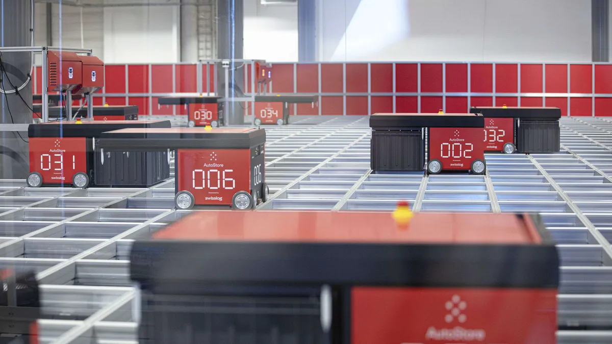 Verkkokauppa.comin varasto­automaattia operoivat punaiset robotit, jotka nostavat ja kuljettavat harmaita tavaralaatikoita kehikon alla olevista pinoista.