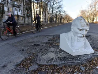 Kuva tammikuulta 2023 Lymanin kaupungista, jossa Leninin patsas peittää taisteluiden aiheuttamaa reikää tiessä.