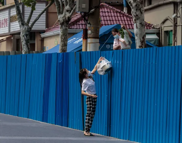 Nainen ojentaa elintarvikkeita karanteeniin joutuneelle naiselle Shanghaissa. Viranomaiset valvovat tarkasti kaduilla liikkumista.