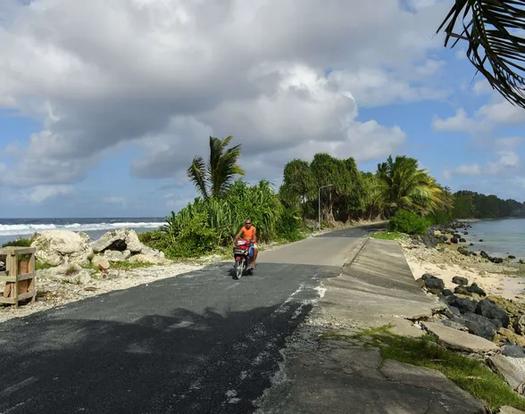 Mies ajaa skootterilla Tuvalun pääkaupunki Funafutin pohjoispuolella saaren kapeimmassa kohdassa. Kuva on vuodelta 2019.