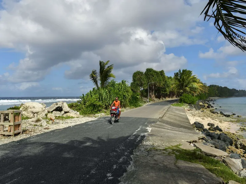 Mies ajaa skootterilla Tuvalun pääkaupunki Funafutin pohjoispuolella saaren kapeimmassa kohdassa. Kuva on vuodelta 2019.
