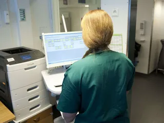 Kuvassa sairaanhoitaja tutkii kiertokärryssä olevaa potilastietojärjestelmää.